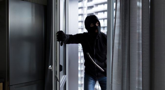 A male thief in a black mask, enters the apartment for robbery, the robber broke the door lock